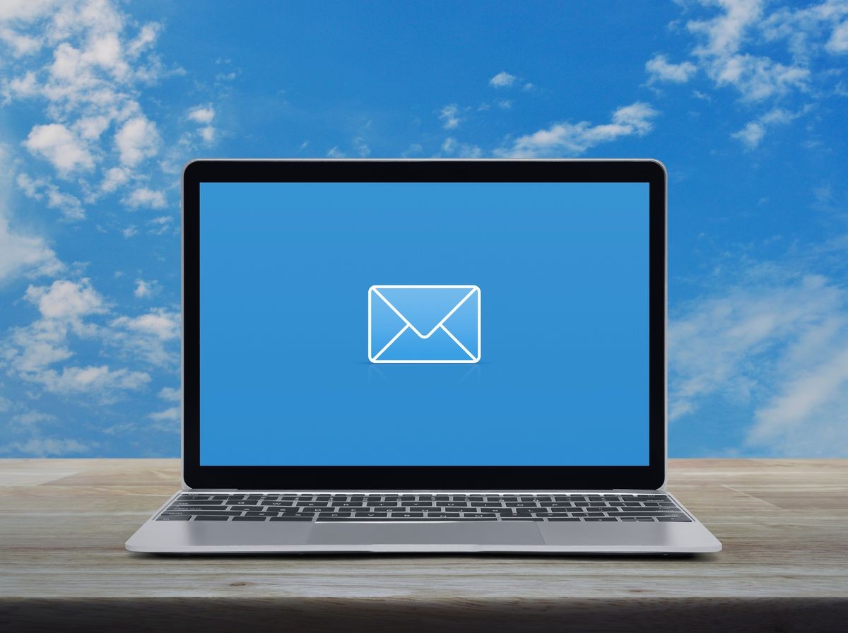 email flat icon with modern laptop computer on wooden table over blue sky with white clouds, Business contact us concept