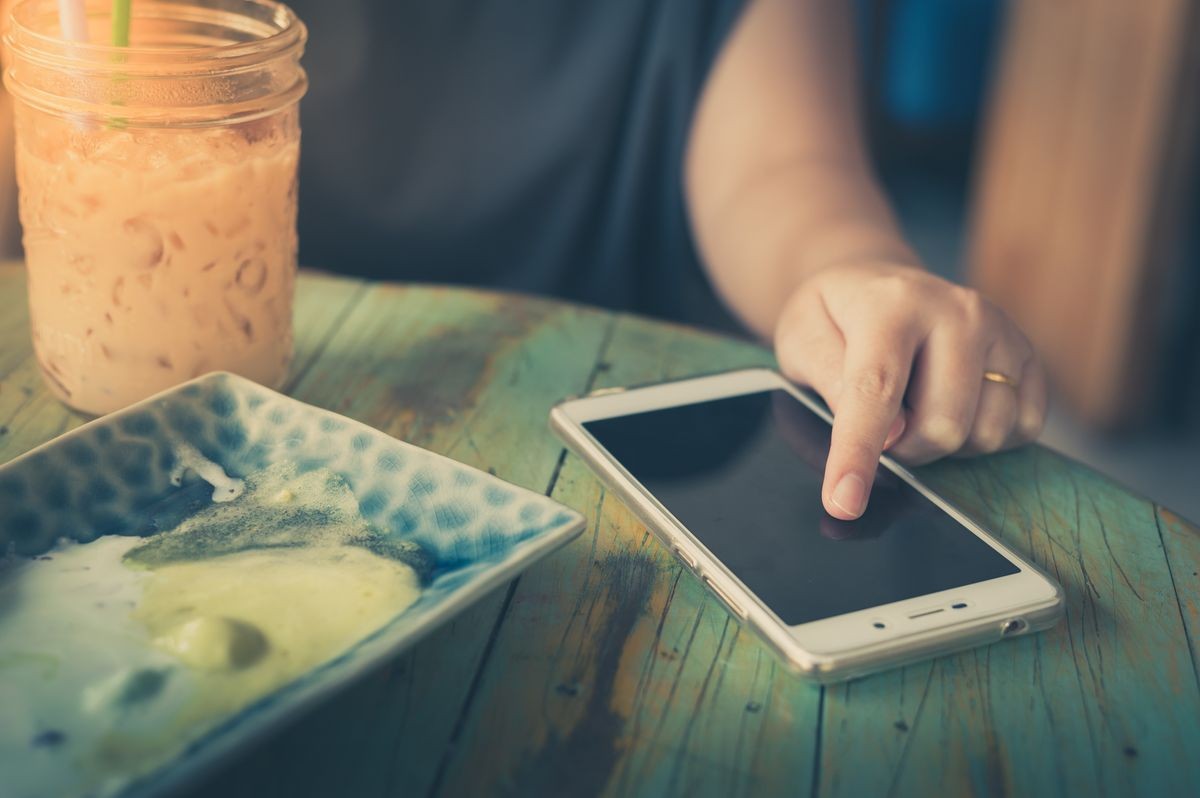 Woman left hand touching on smartphone screen in cafe on weekend afternoon. Trendy lifestyle concept with technology with vintage filter effect